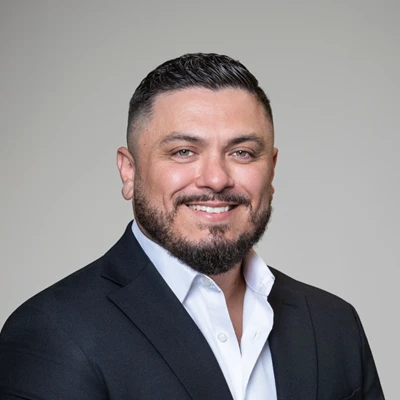 Chiropractor Pierre Quiroz smiling in a black suit.